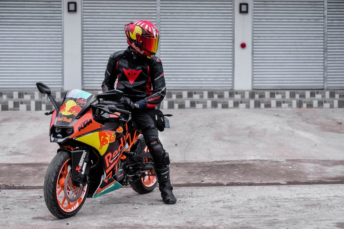 A rider in full protective gear beside a motorcycle